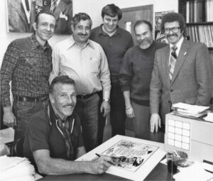 MARCH 29, 1980 Actor Buster Crabbe autographs a "cartoon¬bio" of his career, drawn by artist Joel Bogart, a long-time member of our very first TWTD support staff. Behind Buster, from left, are original Support Staff volunteers Dennis Bubacz, Mort Paradise, Gary Schroder and Joel Bogart.